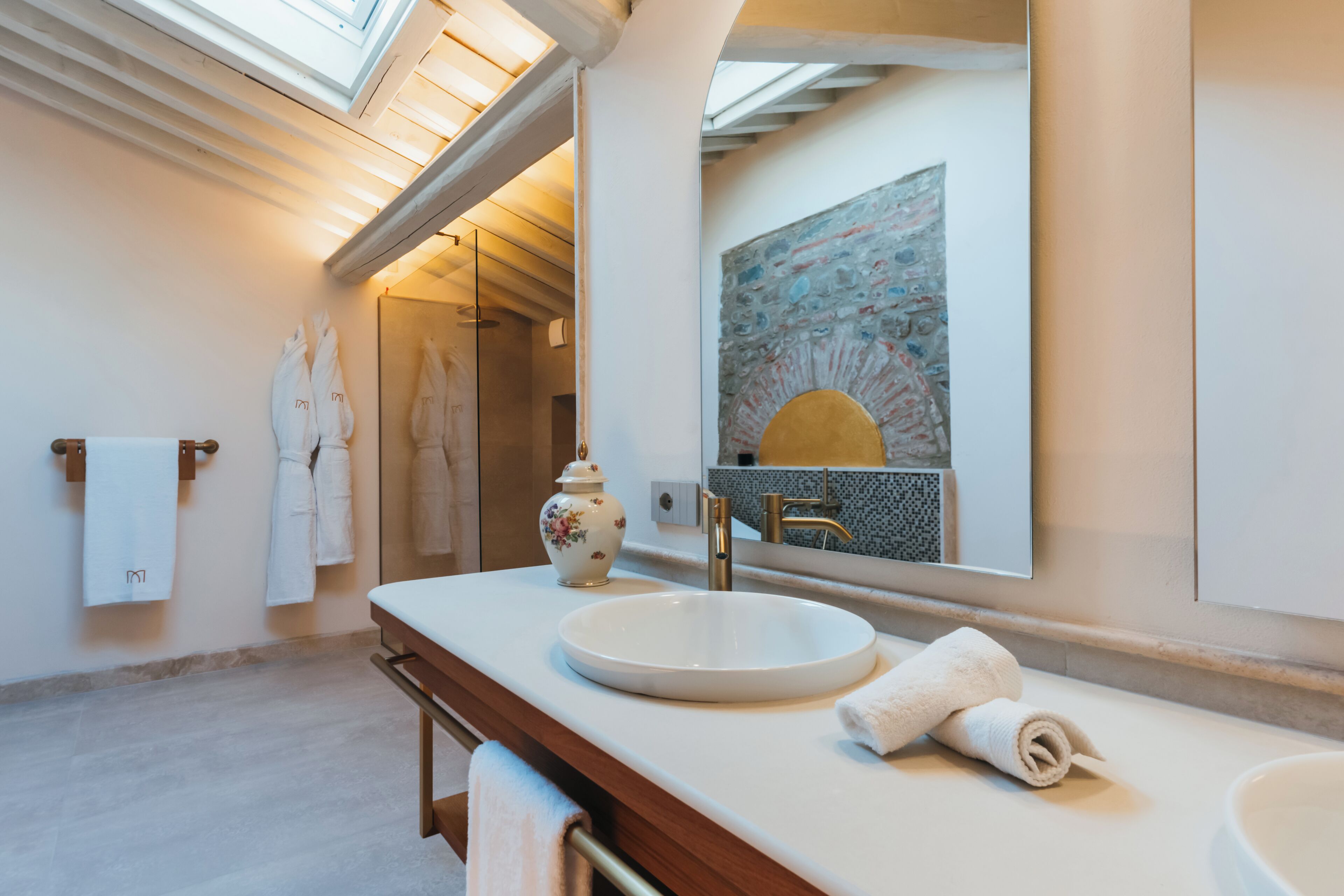 A modern bathroom with a large mirror, a round sink, and a skylight.