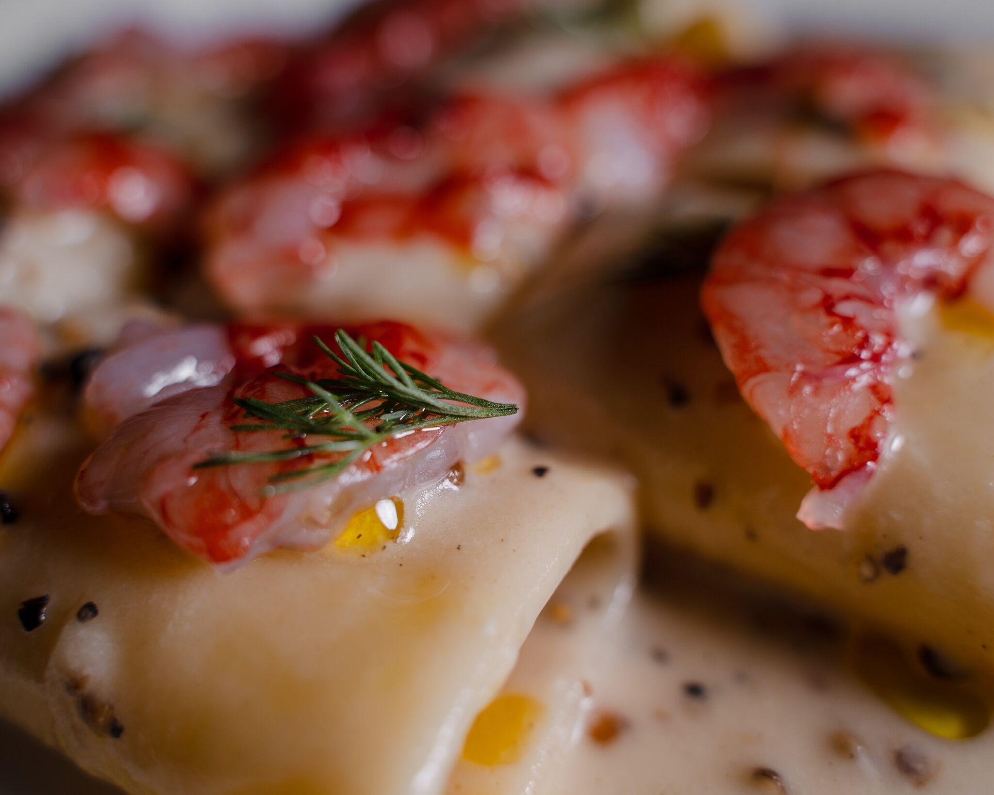 A close-up of a dish with shrimp and a sprig of rosemary on top.
