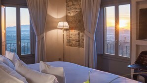 A hotel room with a bed, curtains, a lamp, and a view of the city. - La Monastica Resort & Spa (Buggiano)