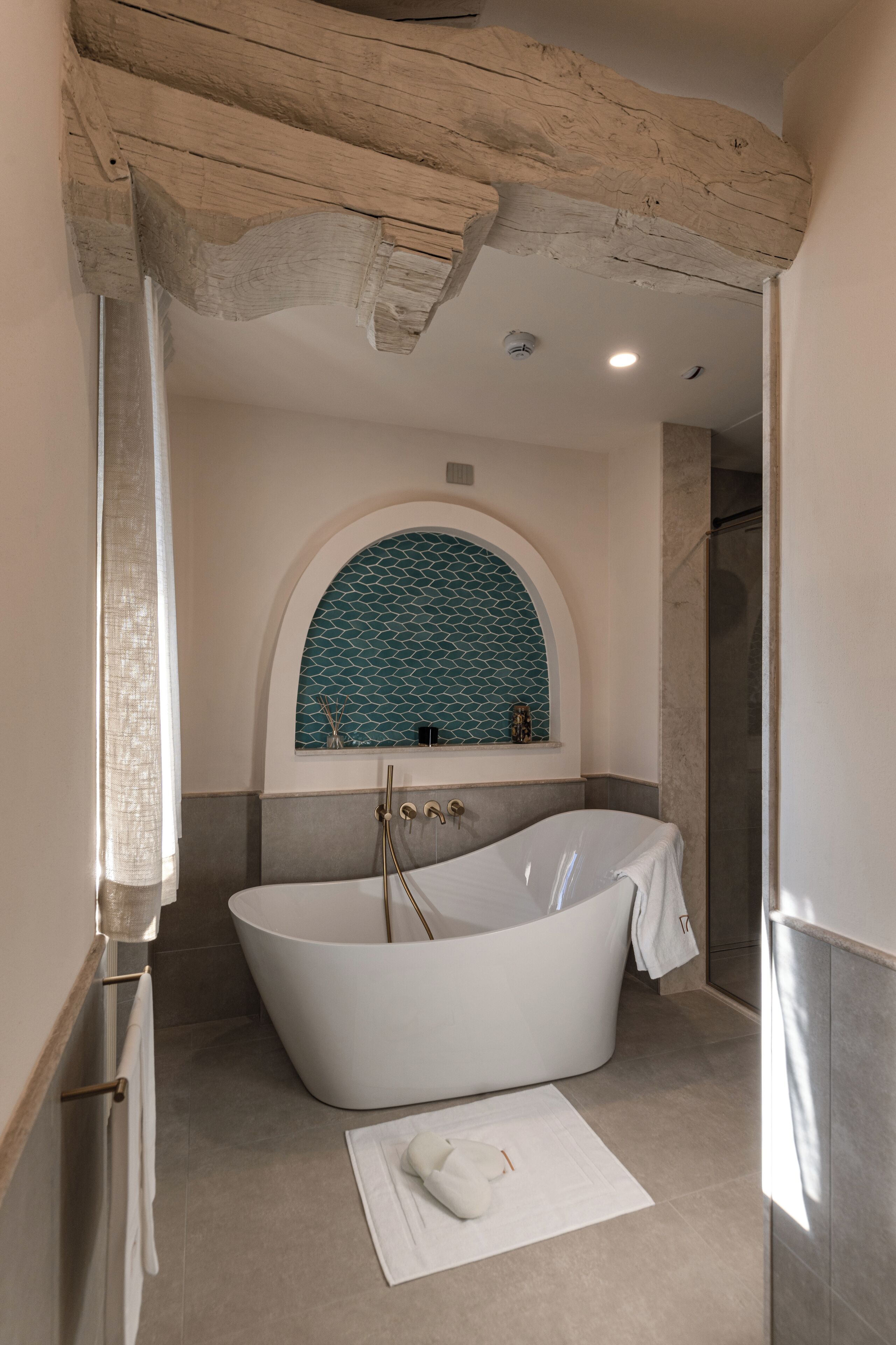 Ein modernes Badezimmer mit einer freistehenden Badewanne, einer gefliesten Duschkabine und einem Fenster mit dekorativem Bogenbogen.