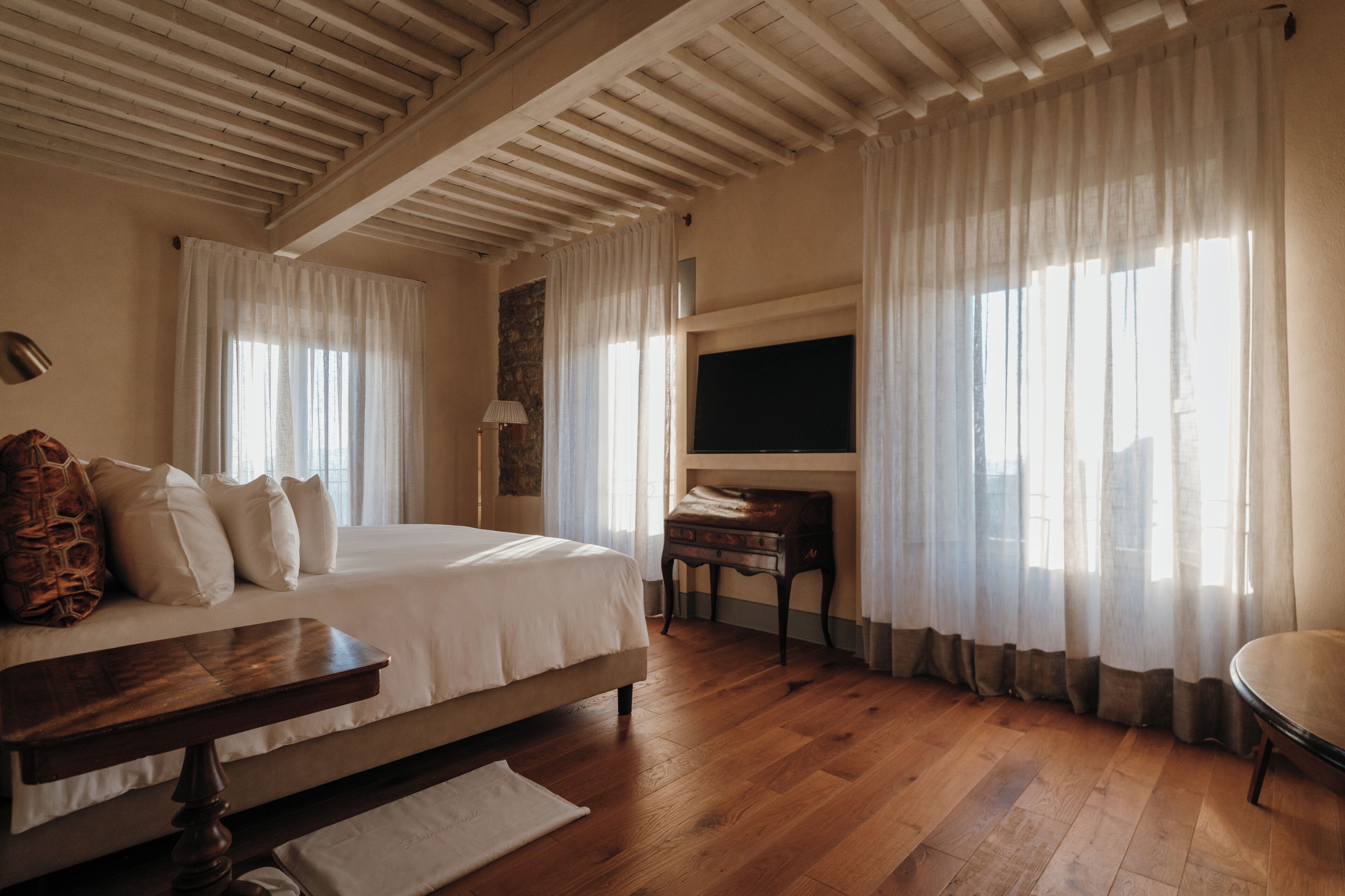 A bedroom with a wooden bed, a nightstand, a desk, and a TV mounted on the wall.