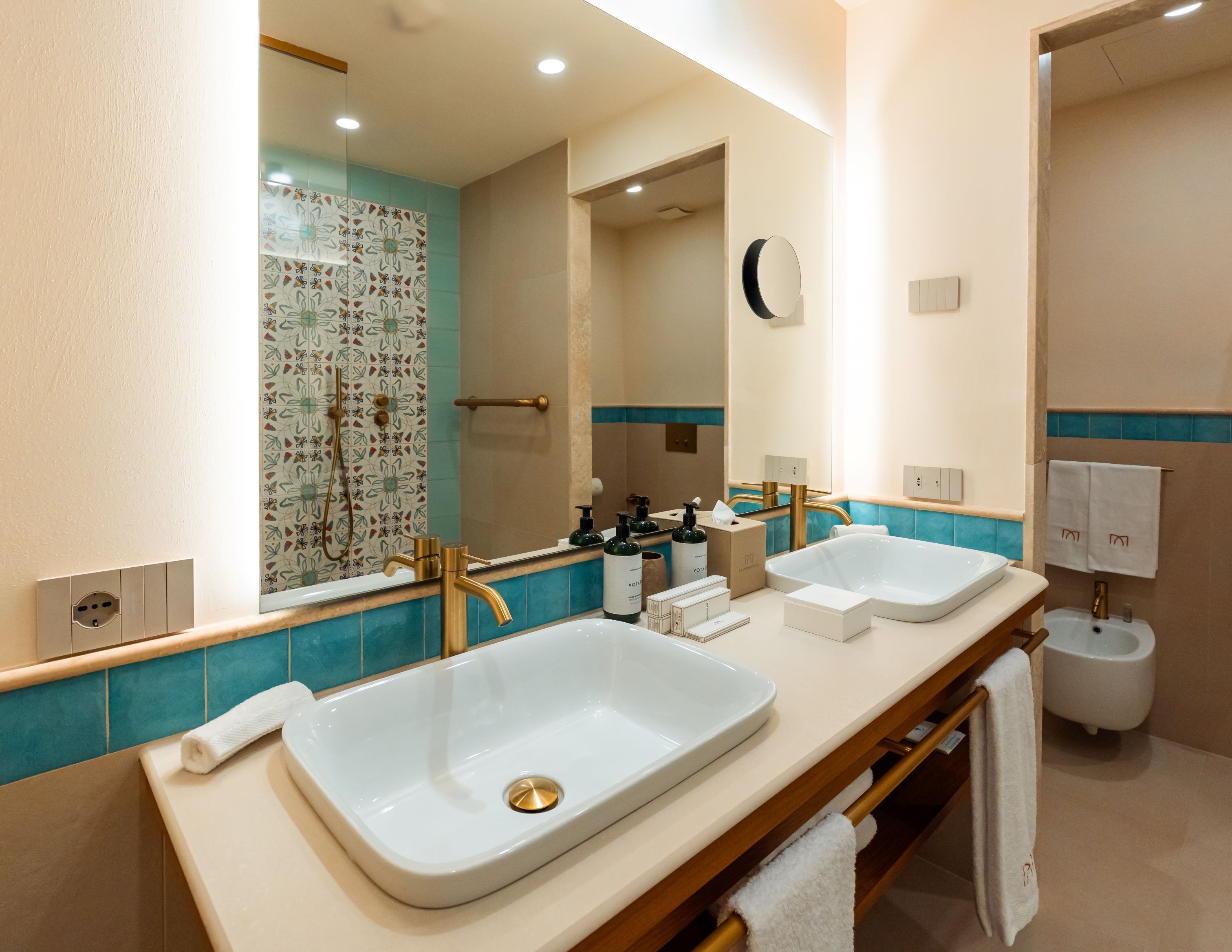 A modern bathroom with two sinks, a large mirror, and a shower area.