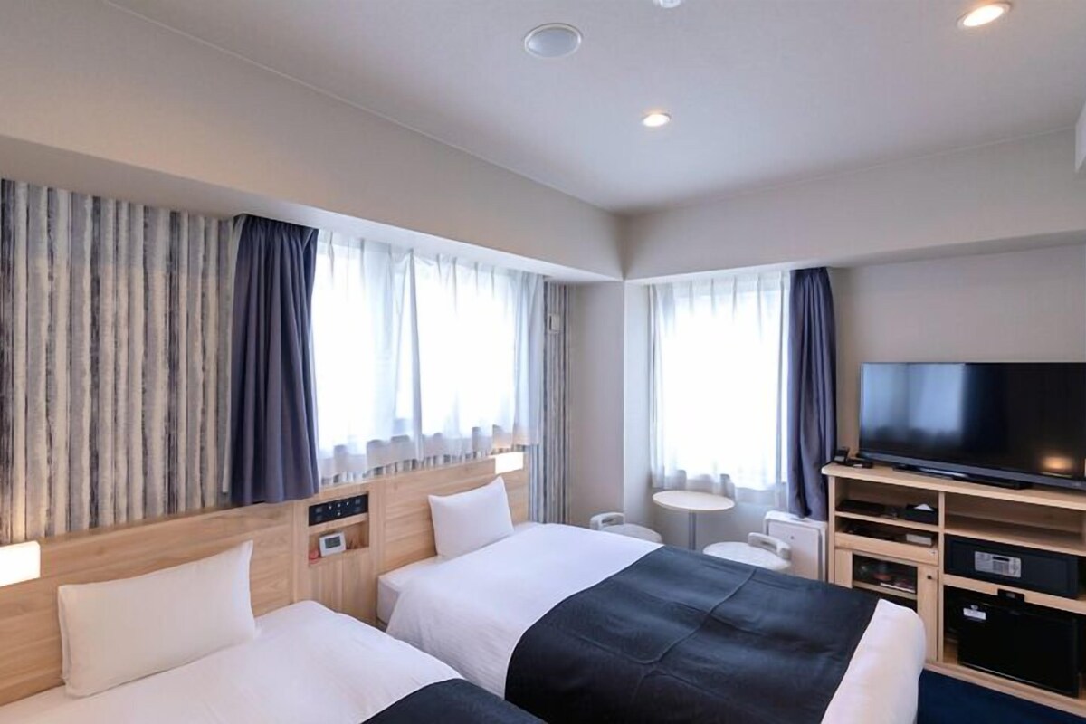 Habitación de hotel con dos camas, televisión, una mesita pequeña y un escritorio con espacio de almacenamiento.