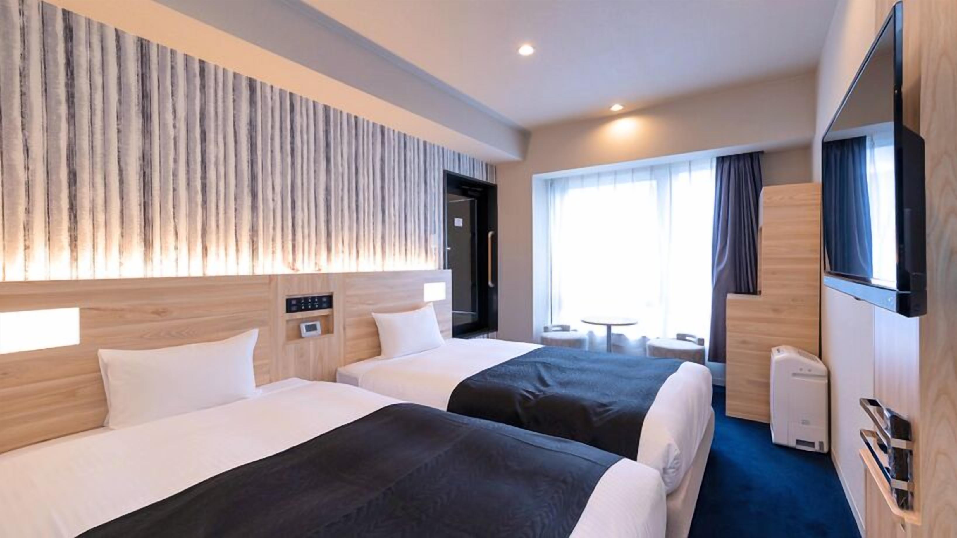 Ein Hotelzimmer mit zwei Betten, einem Fernseher, einer Kaffeemaschine und einer kleinen Sitzecke mit Tisch und Stühlen.