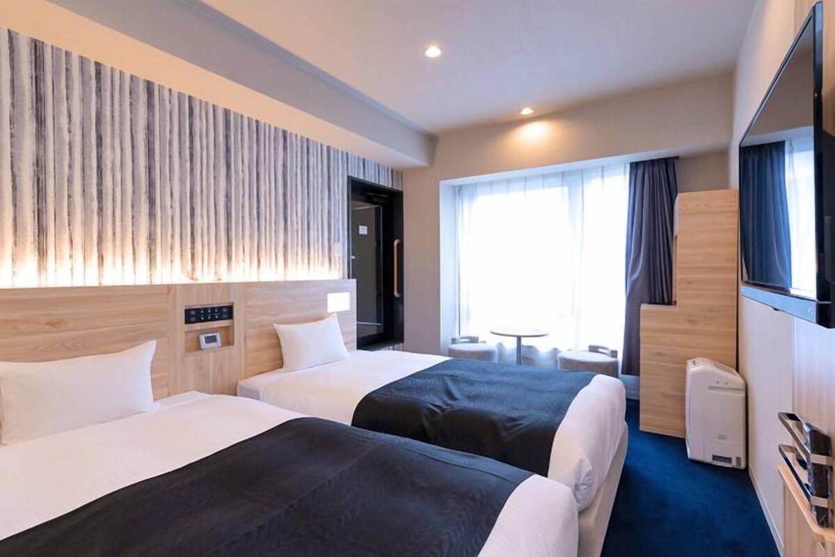 Een hotelkamer met twee bedden, een televisie, een koffiezetapparaat en een zithoekje met een tafeltje en stoelen.