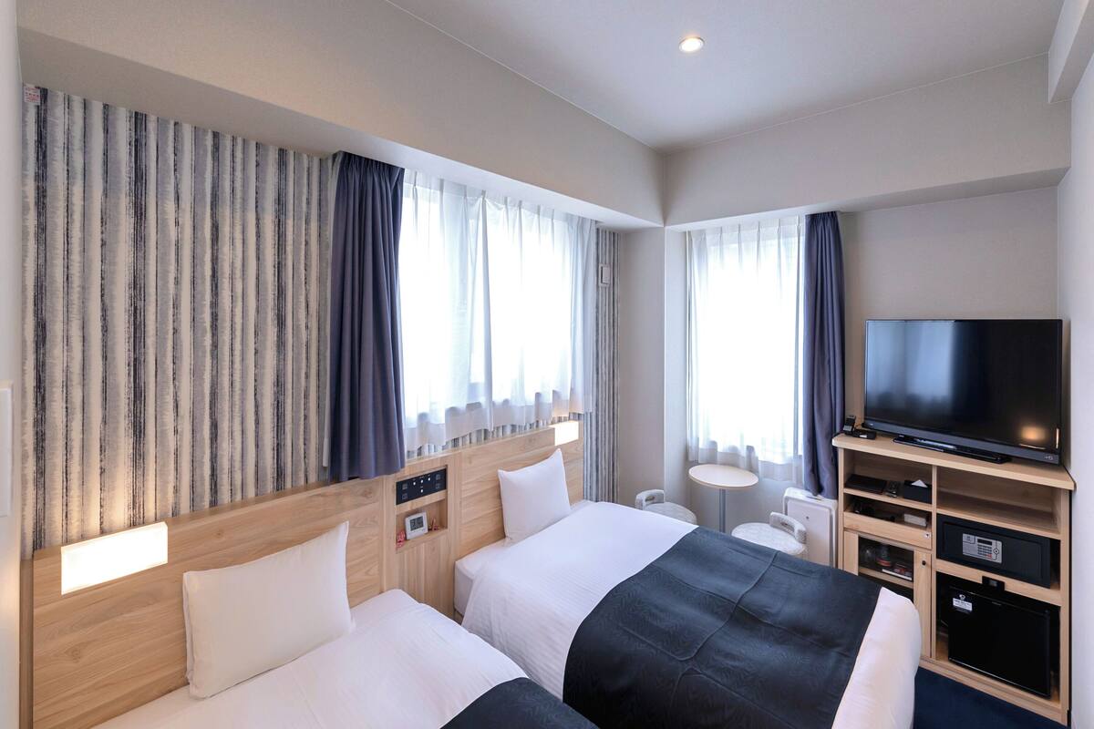 Een hotelkamer met twee bedden, een televisie, een kleine tafel en een bureau met een computer.