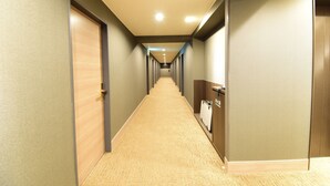 Un pasillo de hotel con pisos alfombrados, puertas de madera y un extintor de incendios montado en la pared.