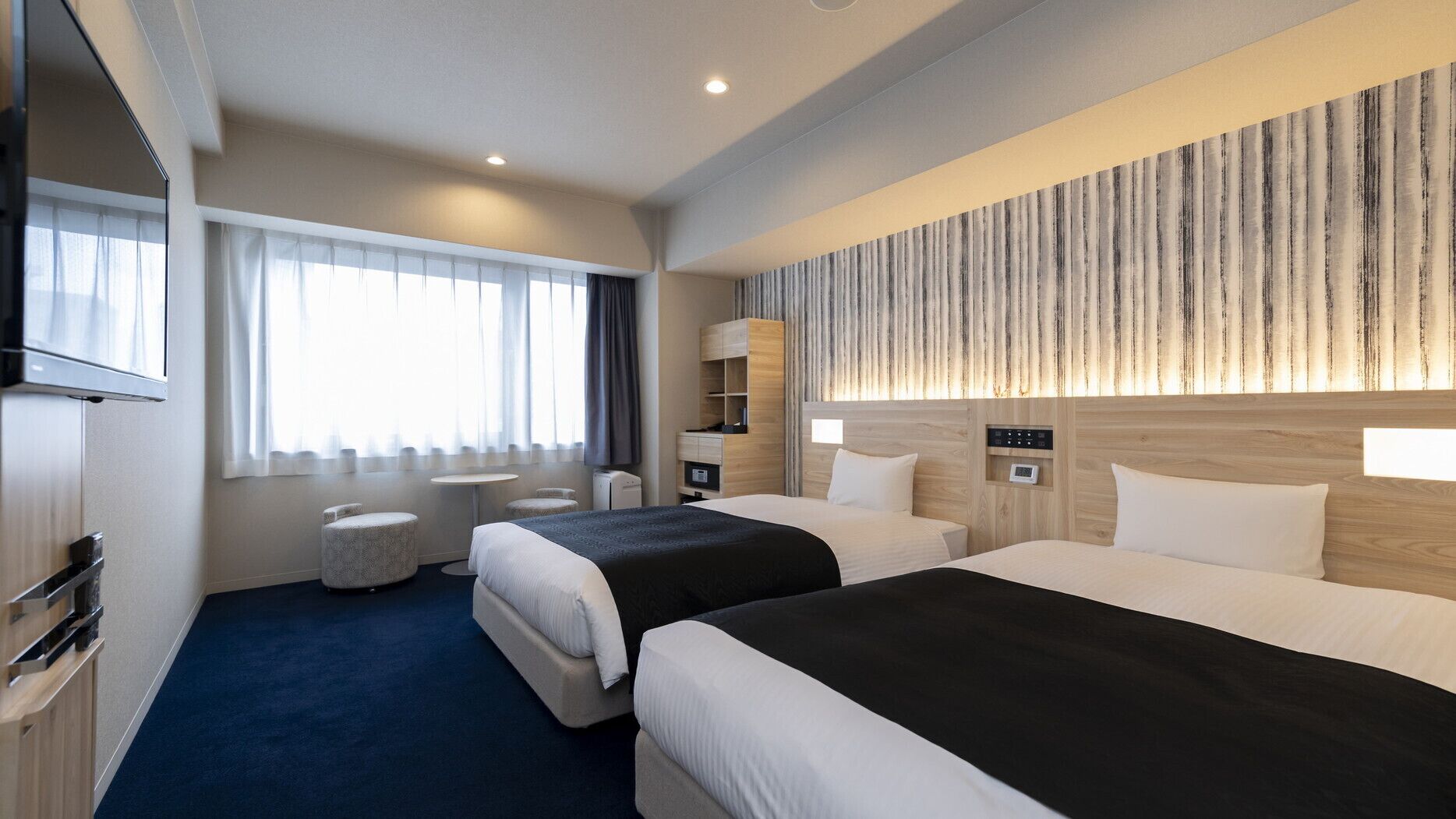 Ein Hotelzimmer mit zwei Betten, einem Fernseher, einem Schreibtisch und einem Fenster mit Vorhängen.