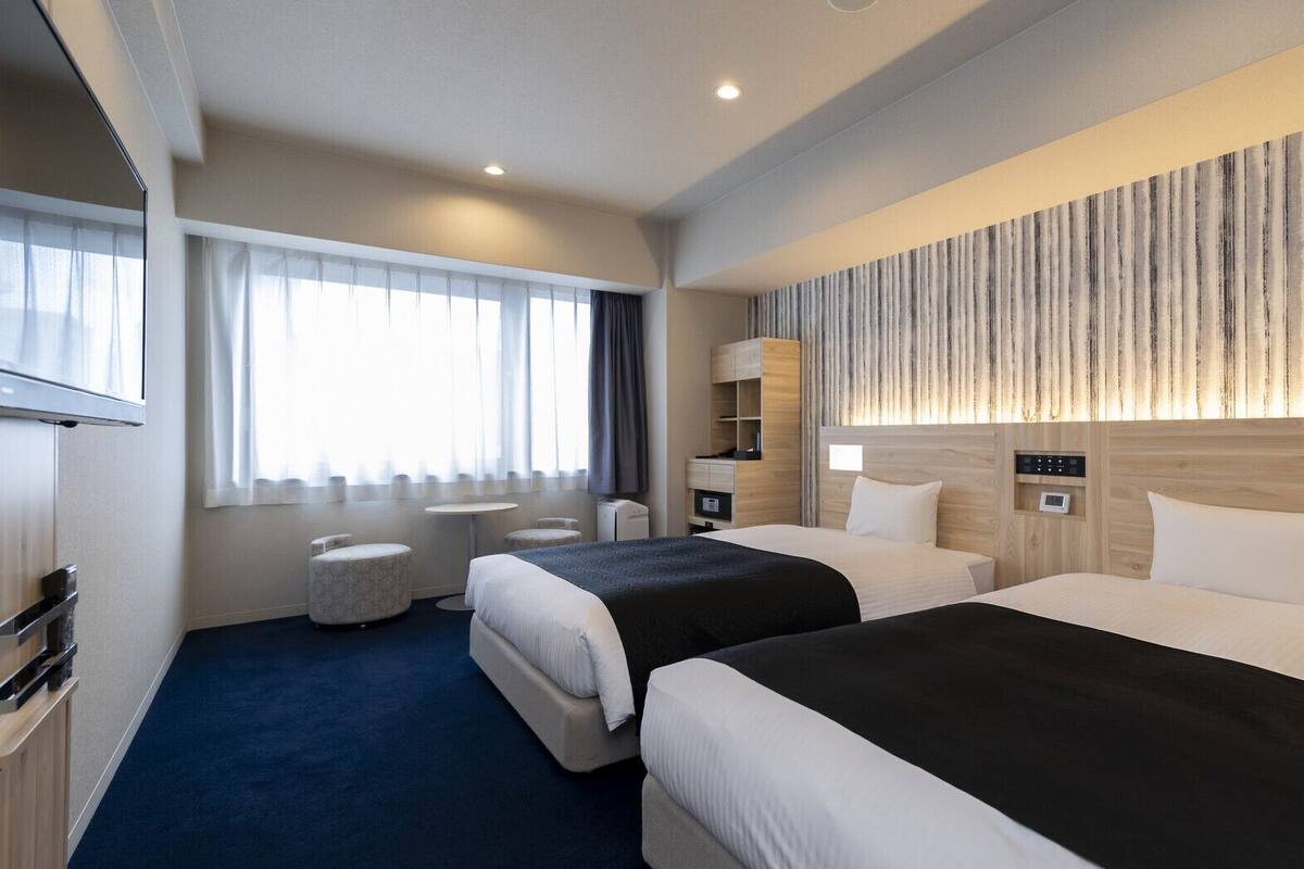 Een hotelkamer met twee bedden, een televisie, een bureau en een raam met gordijnen.