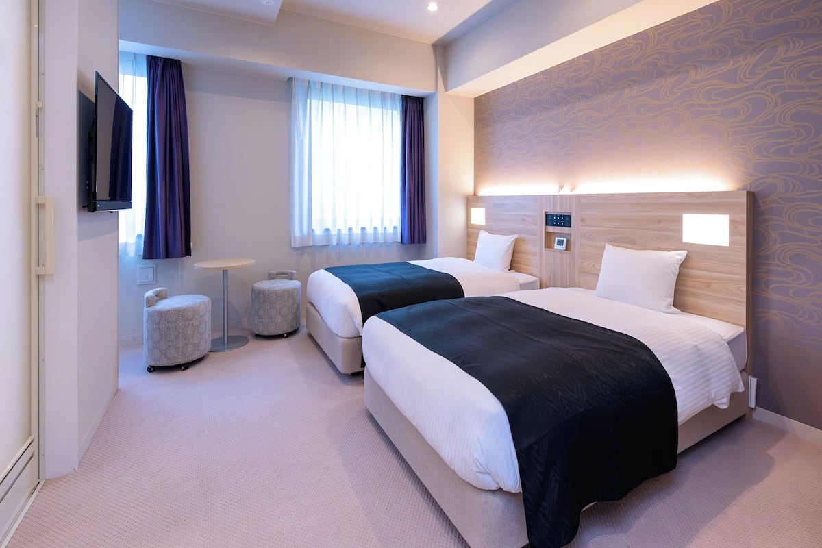 Een hotelkamer met twee bedden, een flatscreen televisie, een klein tafeltje en een raam met gordijnen.