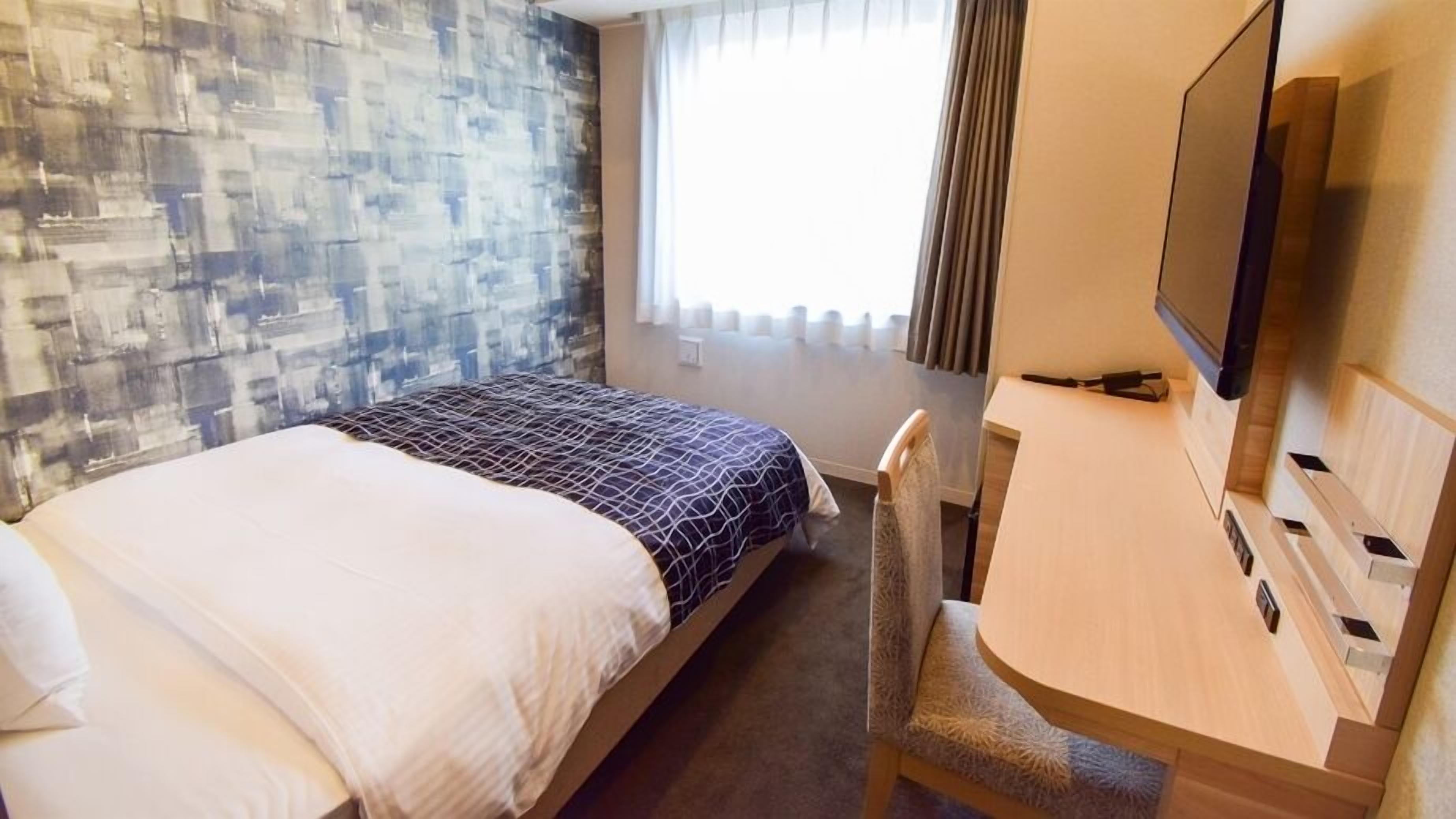 Ein Hotelzimmer mit Bett, Schreibtisch mit Stuhl, Fernseher und einem Fenster mit Vorhängen.