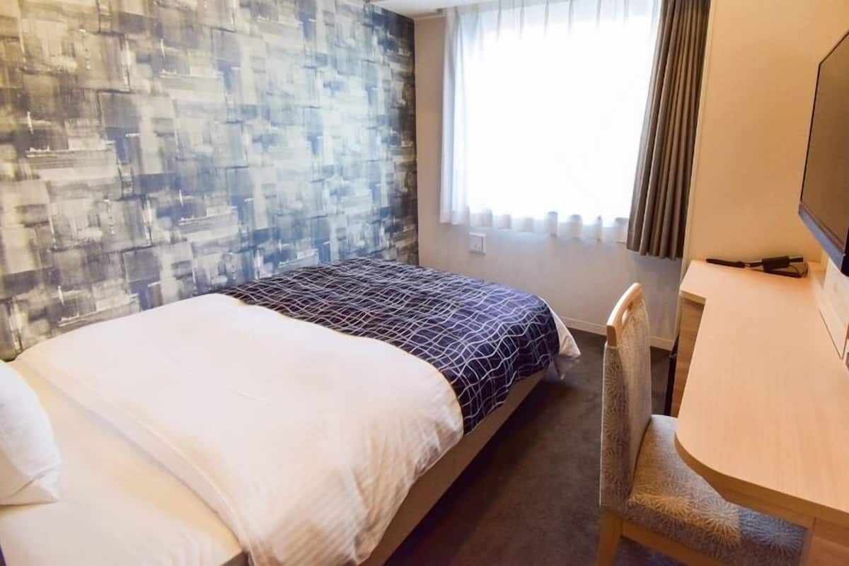 Een hotelkamer met een bed, een bureau met stoel, een televisie en een raam met gordijnen.