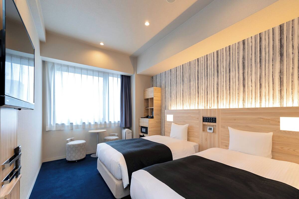 Een hotelkamer met twee bedden, een flatscreen-tv, een klein rond tafeltje, een bank en een houten accentmuur.