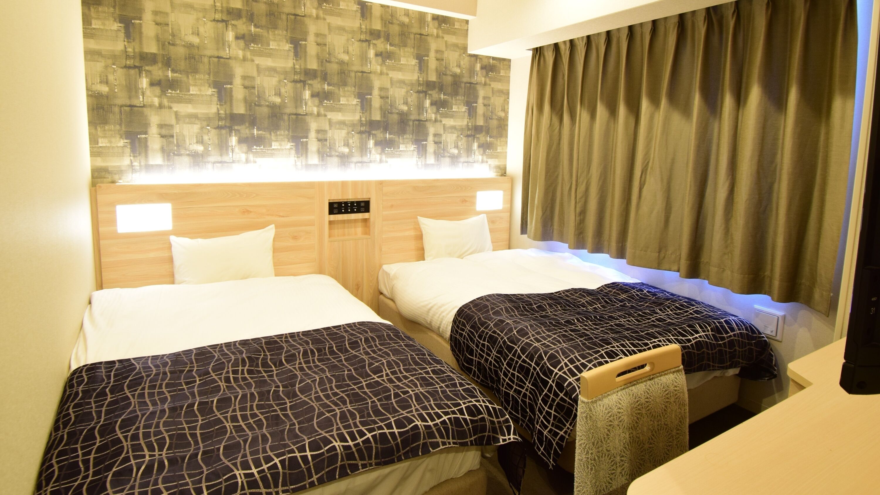 A hotel room with two beds, a wooden headboard, a wall-mounted control panel, and a curtain.