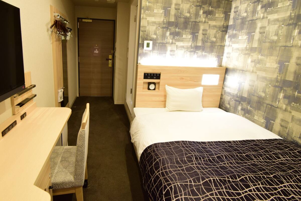 Een hotelkamer met een bed, een bureau, een stoel, een televisie en een klok aan de muur.