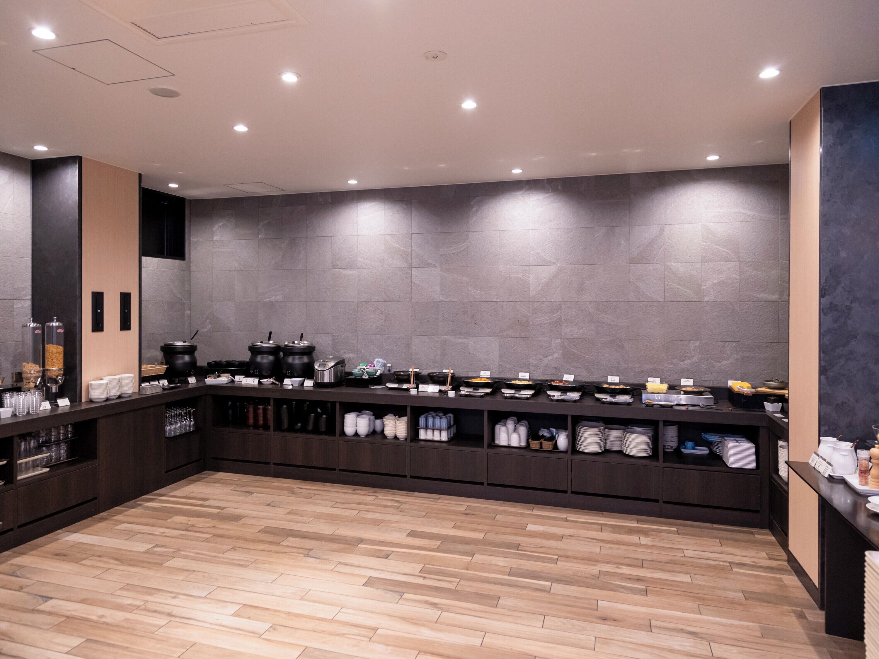 A modern, well-lit kitchen area with a long counter, various cooking appliances, and neatly arranged dishes and utensils.