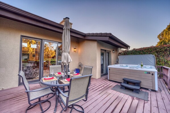 An outdoor deck with a hot tub, a table with chairs, and a covered umbrella.