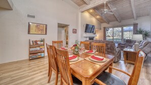 A dining area with wooden tables and chairs, a bookshelf, and a television in the background. - Sedona Bliss at Canyon Mesa Country Club (Sedona)