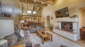 A spacious living room with a fireplace, leather sofas, and a television mounted above it. - Sedona Bliss at Canyon Mesa Country Club (Sedona)