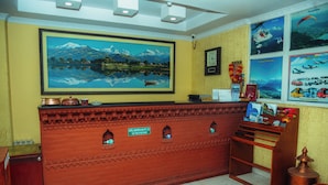 A reception desk with a framed landscape painting, a clock, and a sign indicating the hotel name and address. - Hotel Gantabya Inn (Pokhara)