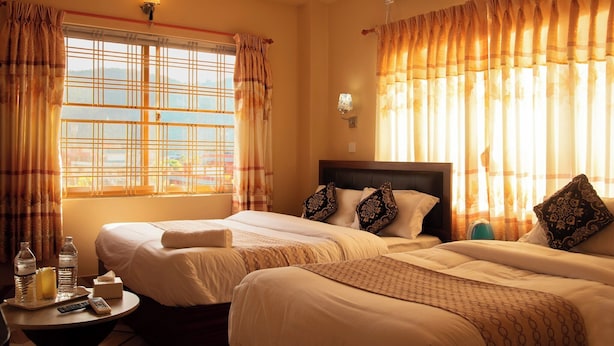 A hotel room with two beds, a bedside table with a bottle of water and a remote control, and a wall-mounted air conditioner. - Hotel Gantabya Inn (Pokhara)