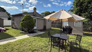 A backyard with a patio table and chairs, a barbecue grill, and a large umbrella.