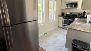 A kitchen with a stainless steel refrigerator, a microwave, a stove, and a trash bin.