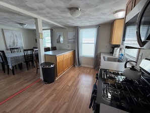 A kitchen with wooden cabinets, a gas stove, a sink, and a dining area with a table and chairs. - This house is a 1 bedroom(s), 1 bathrooms, located in Warwick, RI. (Warwick)