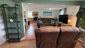 A living room with a brown leather sofa, a TV, and a kitchen in the background.