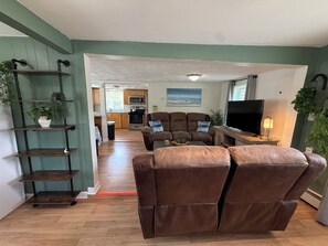 Ein Wohnzimmer mit braunem Ledersofa, einem Fernseher und einer Küche im Hintergrund.