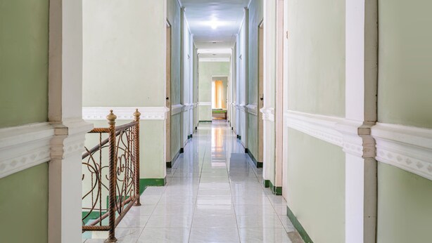 A long, narrow hallway with white tiled floors and green walls, leading to a room with a window and curtains. - Capital O 93949 Hotel Popuci By Pupa Hospitality (Cilimus)