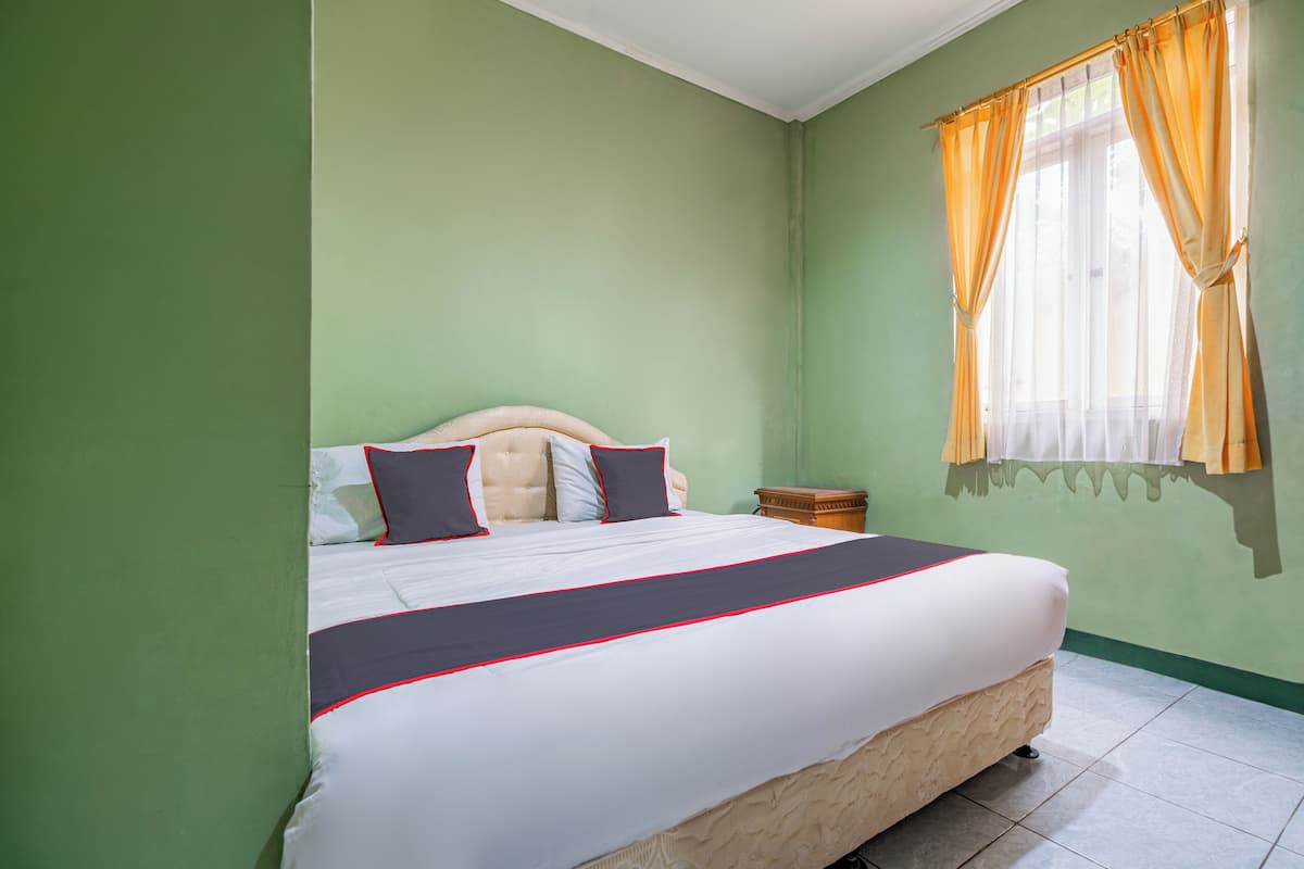 A bedroom with a large bed, green walls, and a window with orange curtains.