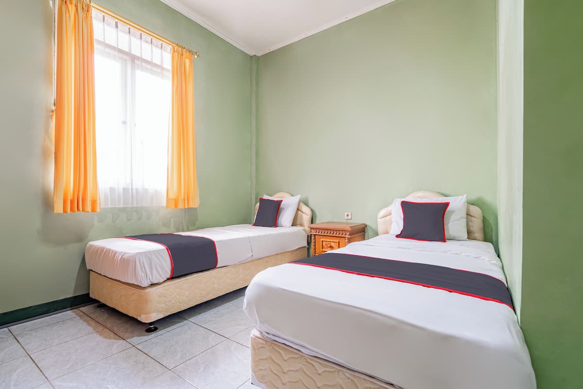 A room with two beds, each with a mattress and pillows, a nightstand, and a window with curtains.