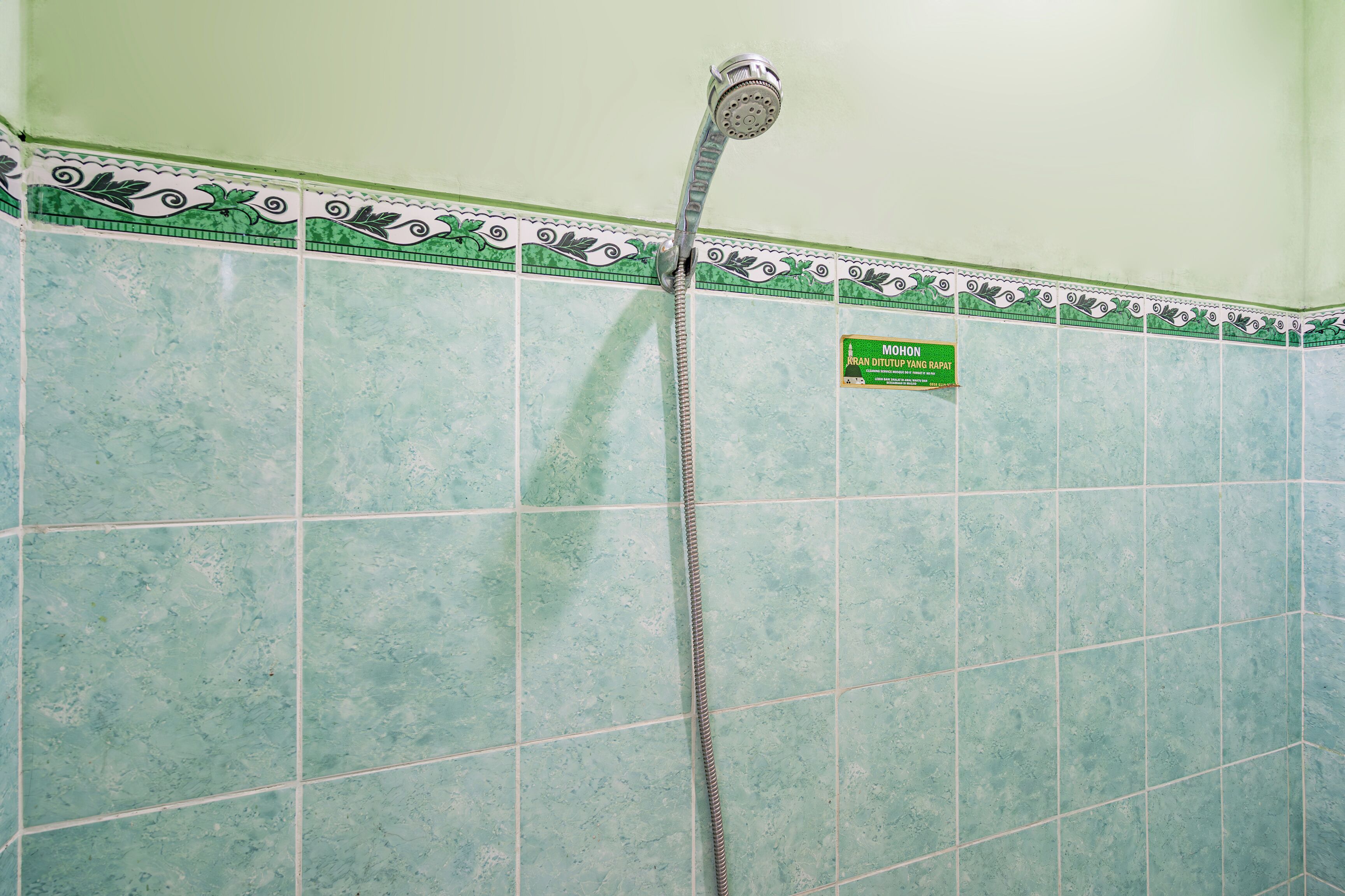 Une salle de bain avec une douche, des carreaux verts et un panneau indiquant une température de l’eau de 40 degrés Celsius.