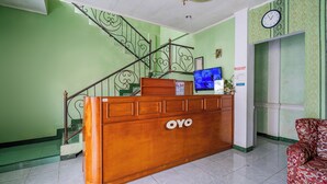 A reception desk with a wooden finish and the logo "OYO". A staircase with ornate metal railings is visible to the left. - Capital O 93949 Hotel Popuci By Pupa Hospitality (Cilimus)