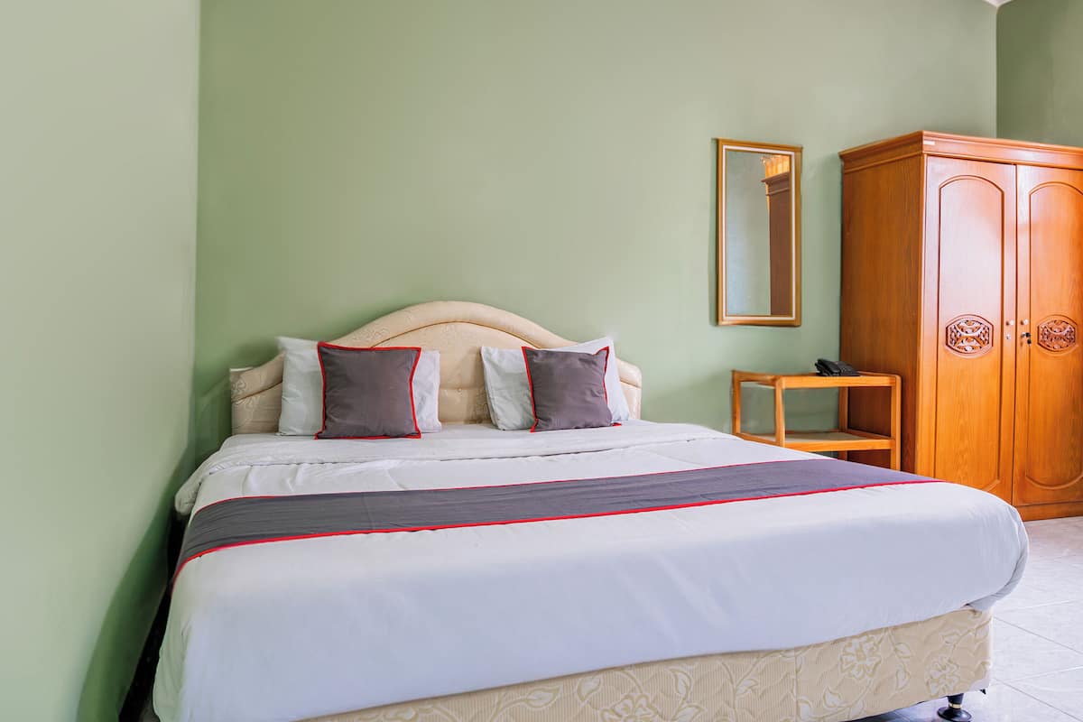 A neatly made bed with a headboard, a wooden wardrobe, and a small bedside table with a phone.