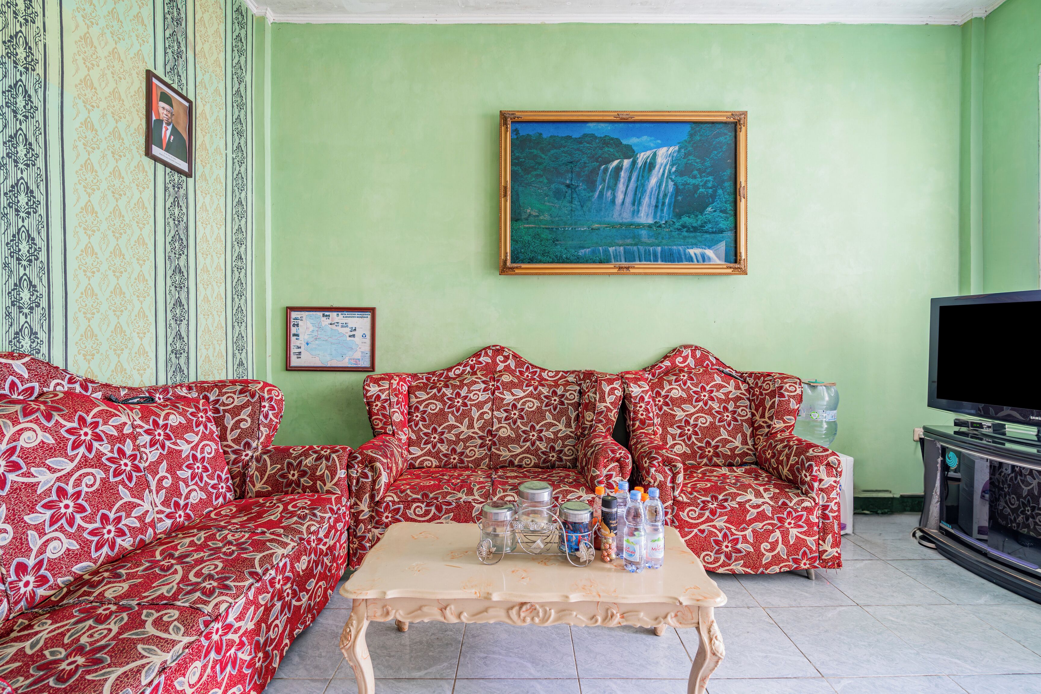 Una sala de estar con un conjunto de sofá, una mesa de centro, un televisor y un cuadro con una cascada.