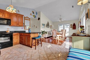 A spacious kitchen with wooden cabinets, a black stove, and a bar area with stools. - Seaing is Believing | Surf City, NC | 4 Bedrooms | Short Walk to Beach (Surf City)