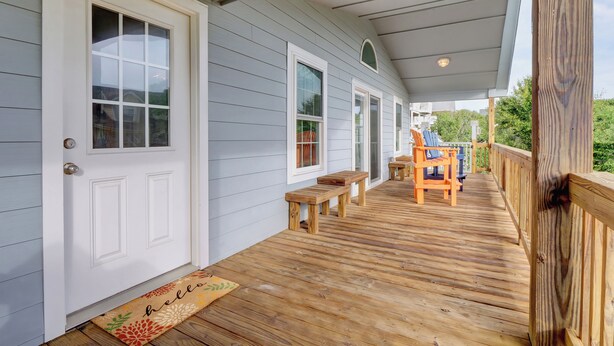 A covered wooden deck with a bench and a chair, a white door, and a doormat. - Seaing is Believing | Surf City, NC | 4 Bedrooms | Short Walk to Beach (Surf City)