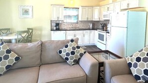 A compact living space with a kitchenette, a sofa with patterned cushions, and a dining area with a table and chairs. - 2 bathroom 1 bath Cottage (Rockport)