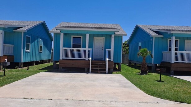 A row of blue mobile homes with white railings, a concrete driveway, and a small palm tree. - 2 bathroom 1 bath Cottage (Rockport)