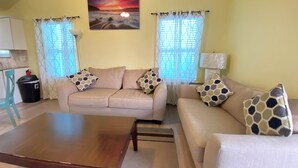Un salon avec un canapé beige, une table basse en bois et un tableau représentant un coucher de soleil.