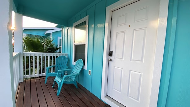 Une véranda avec une porte blanche, des murs turquoise et deux fauteuils Adirondack turquoise.
