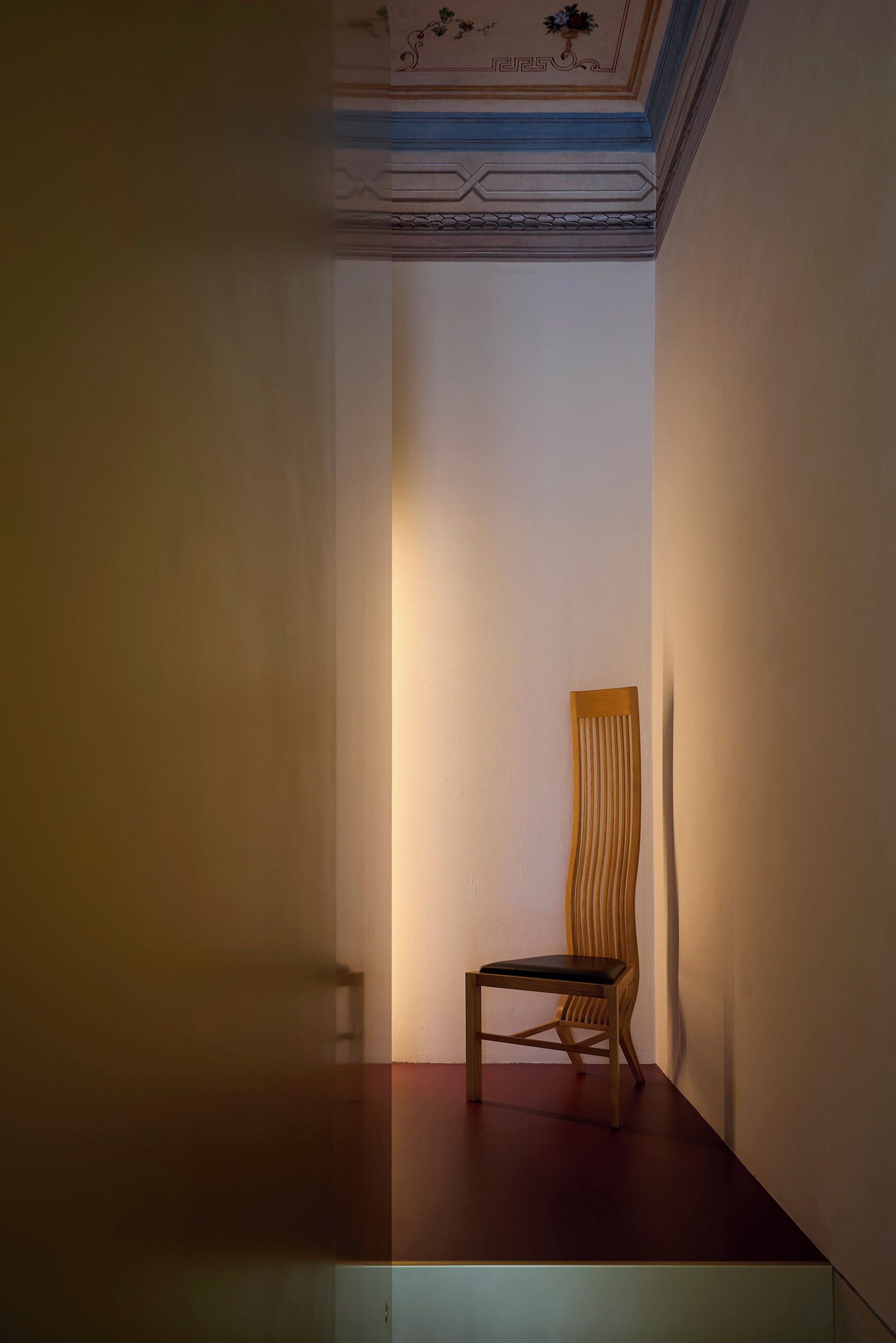 A narrow hallway with a wooden chair and a light source on the wall.