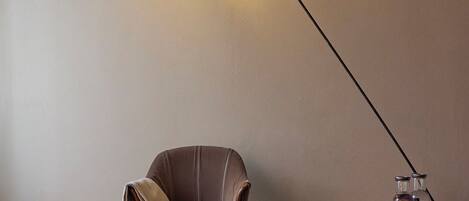 A room with a brown leather armchair, a small side table with a magazine, a floor lamp, and a tray with two glass bottles.