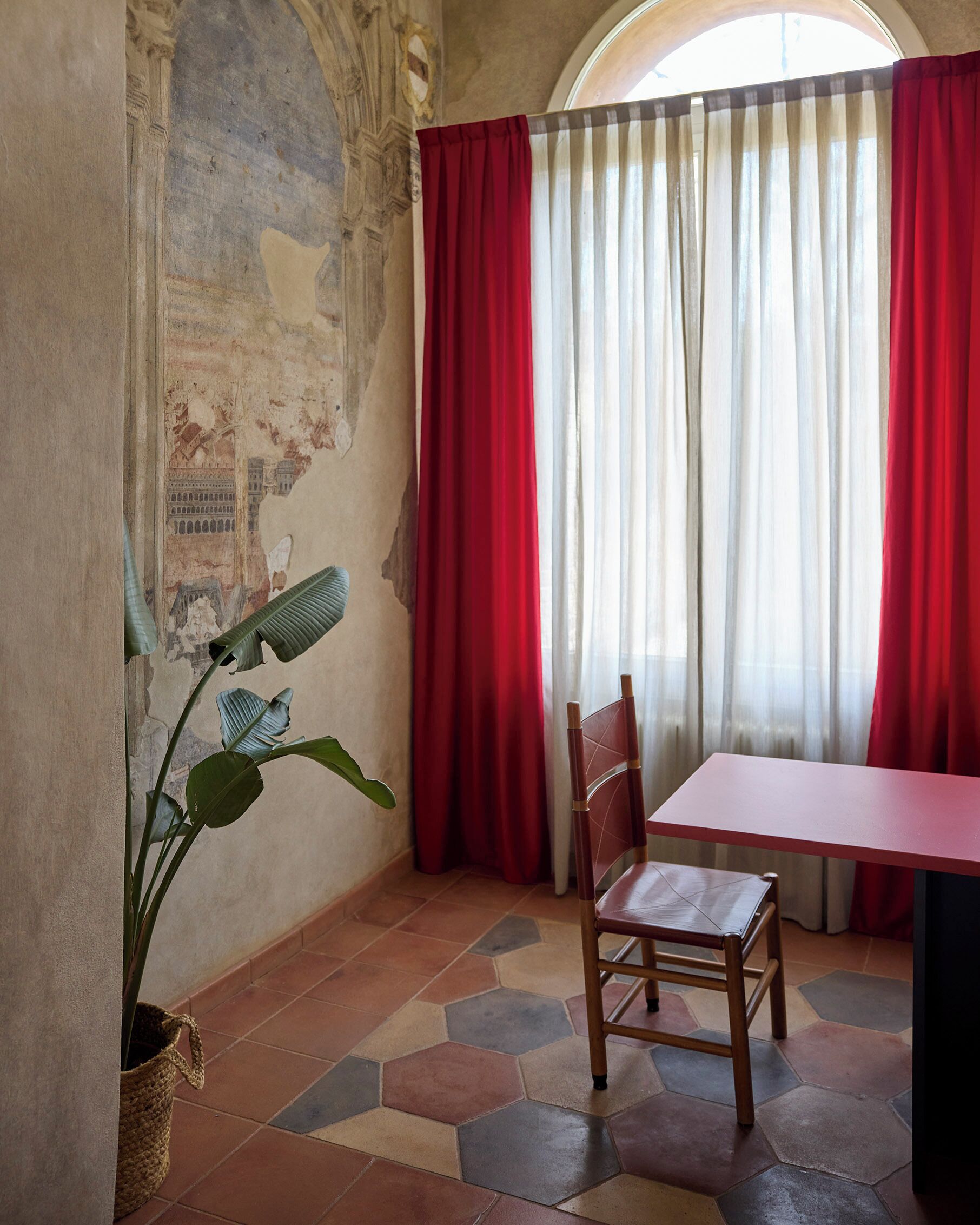 A room with a tiled floor, a wooden chair, a table, red curtains, and a wall with a mural.
