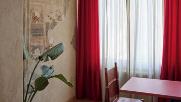 A room with a tiled floor, a wooden chair, a table, red curtains, and a wall with a mural.