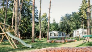 A playground with a slide, a swing set, and a sandbox with toys. - Waldhaus 2 mit Whirlpool - Ferienhäuser Insel Usedom - Direkt am Achterwasser! (Lütow)