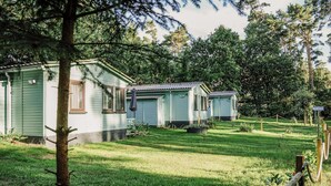 A row of small, light green cabins with a grassy yard and trees in the background. - Waldhaus 2 mit Whirlpool - Ferienhäuser Insel Usedom - Direkt am Achterwasser! (Lütow)