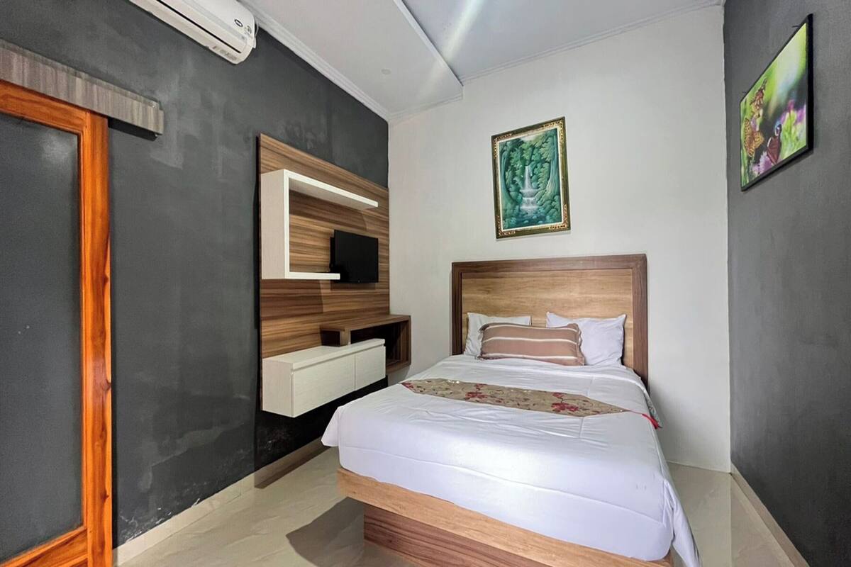 Une chambre d’hôtel avec un lit, une télévision, une tête de lit en bois, une étagère fixée au mur et un tableau.